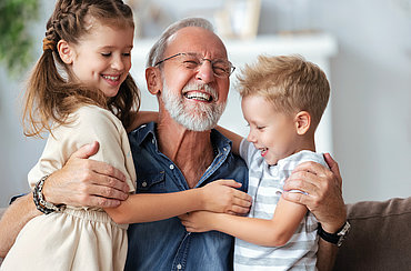 Ein älterer Herr lacht und umarmt zwei Kinder