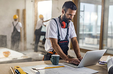 Ein Mann in Arbeitsklamotten arbeitet am Laptop